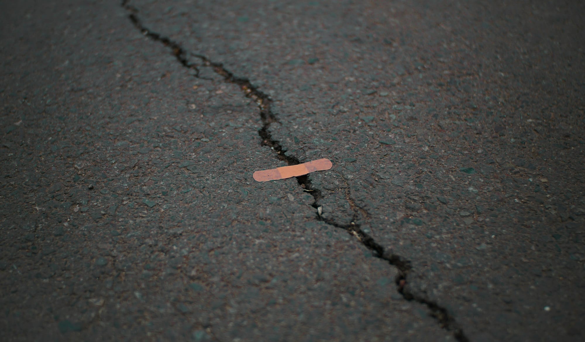 A photo of a crack on dark ground with a piece of plaster connecting both sides.